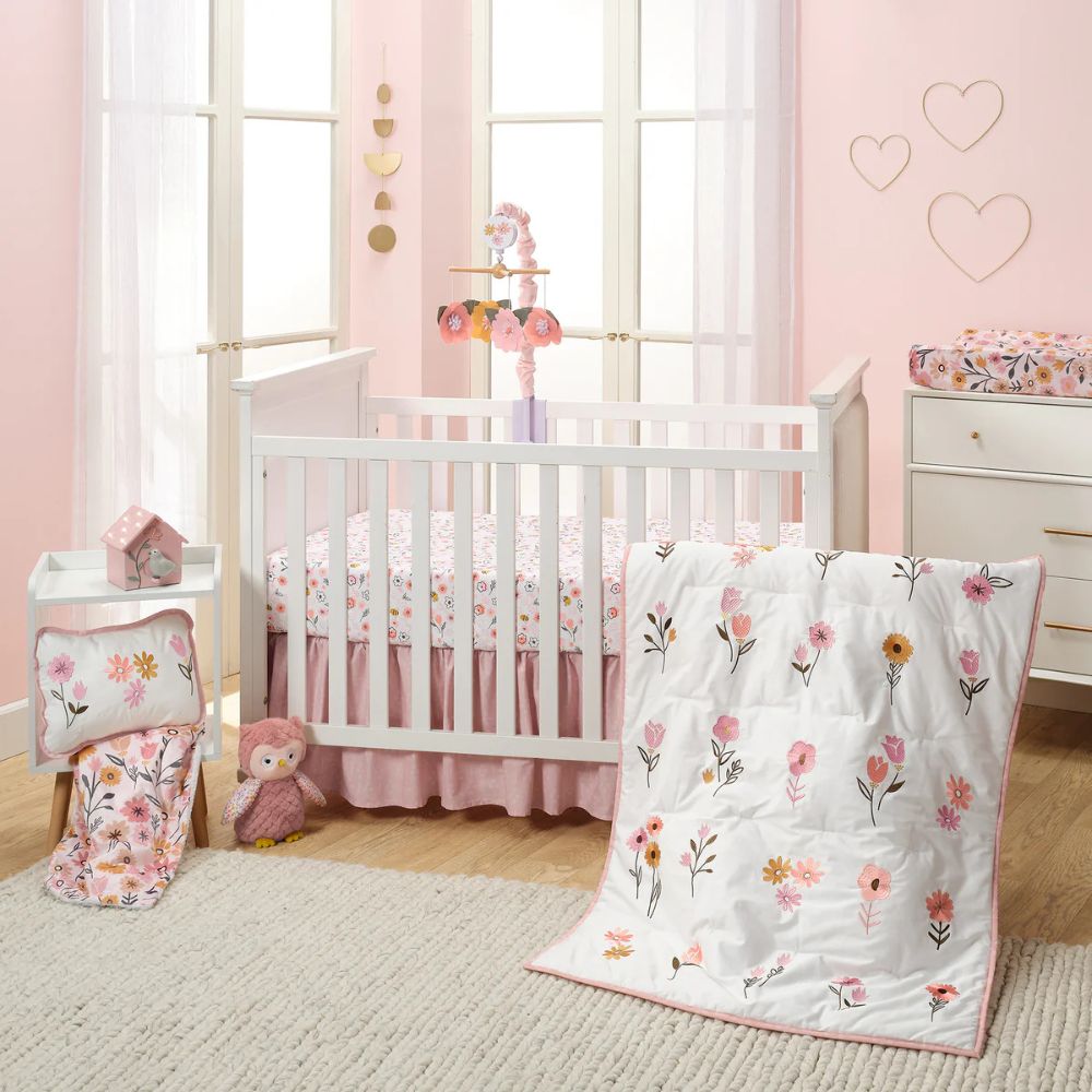 Baby crib with floral bedding in a nursery with pink walls and a window.