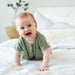 Baby in a green outfit sitting on a white bed