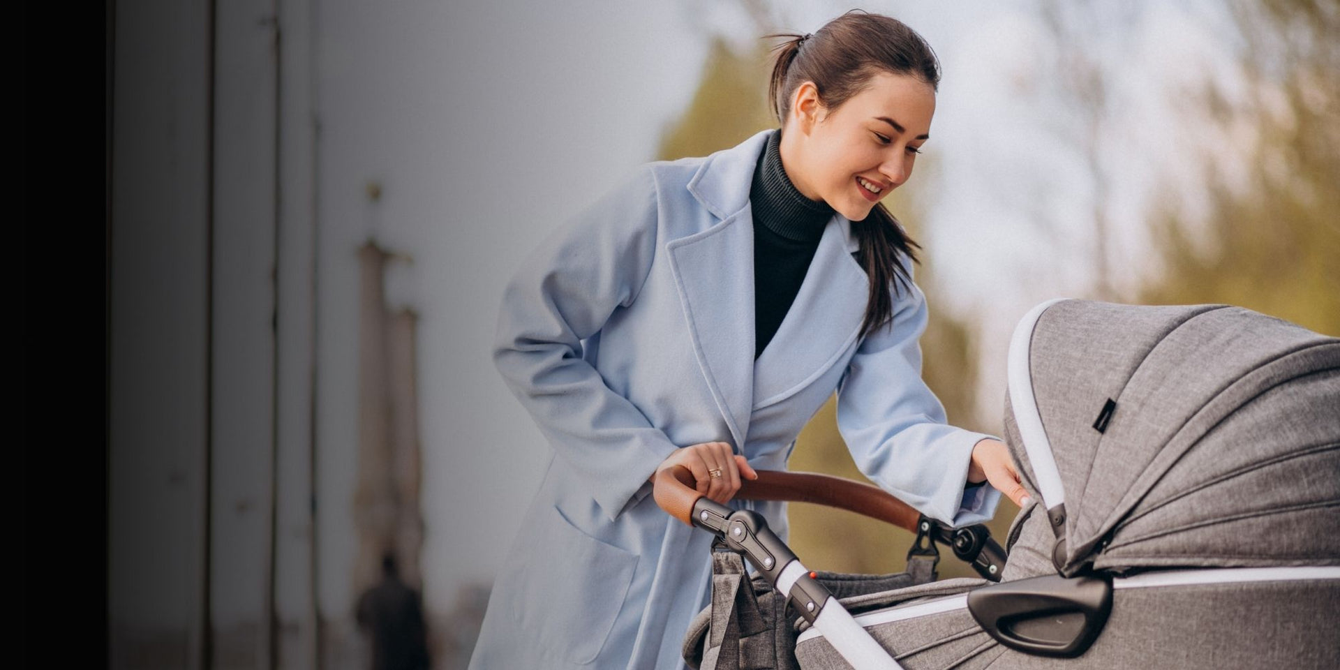 Woman in a light blue coat pushing a gray stroller outdoors.